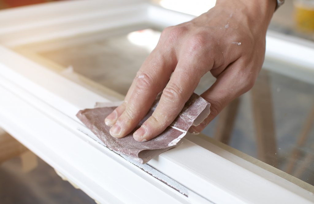 Sanding a window frame with sand paper