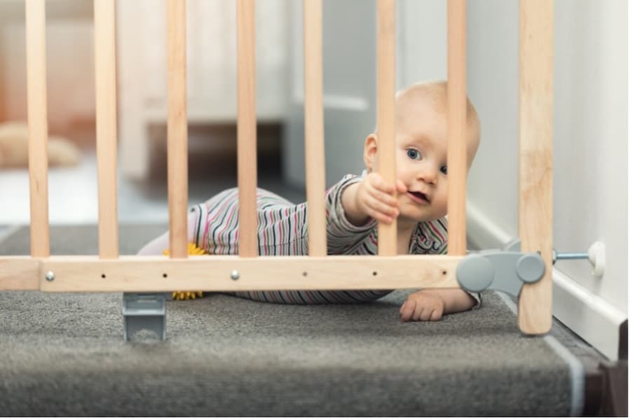 A baby crawling on the floor behind a wooden gate